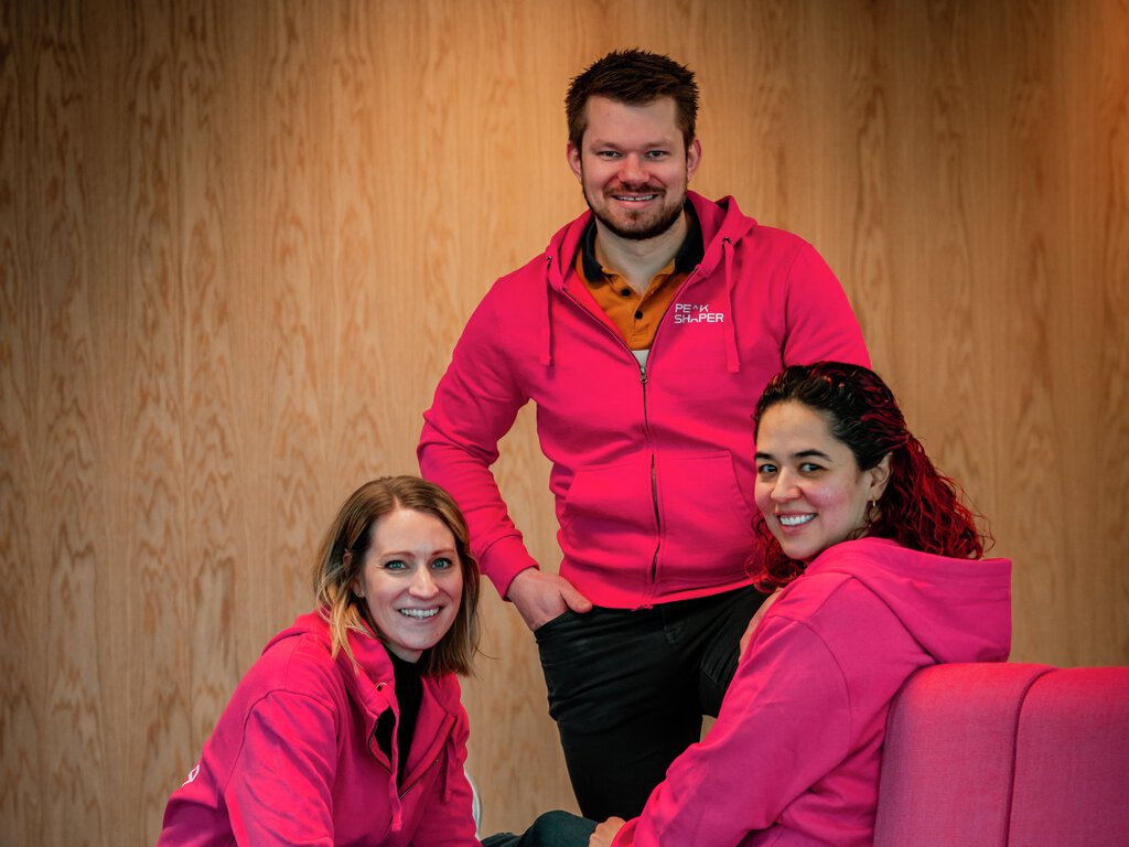 3 kollegaer i rosa hettejakker sitter på rosa sofa