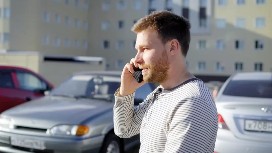 Mand taler i mobiltelefon på parkeringsplads