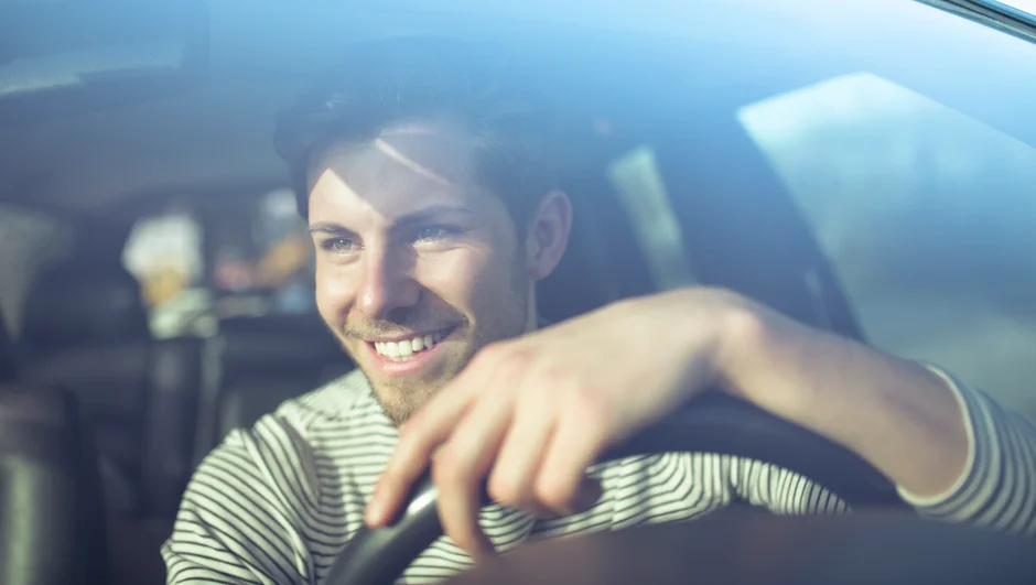 Mand sidder bag rattet i en bil og smiler