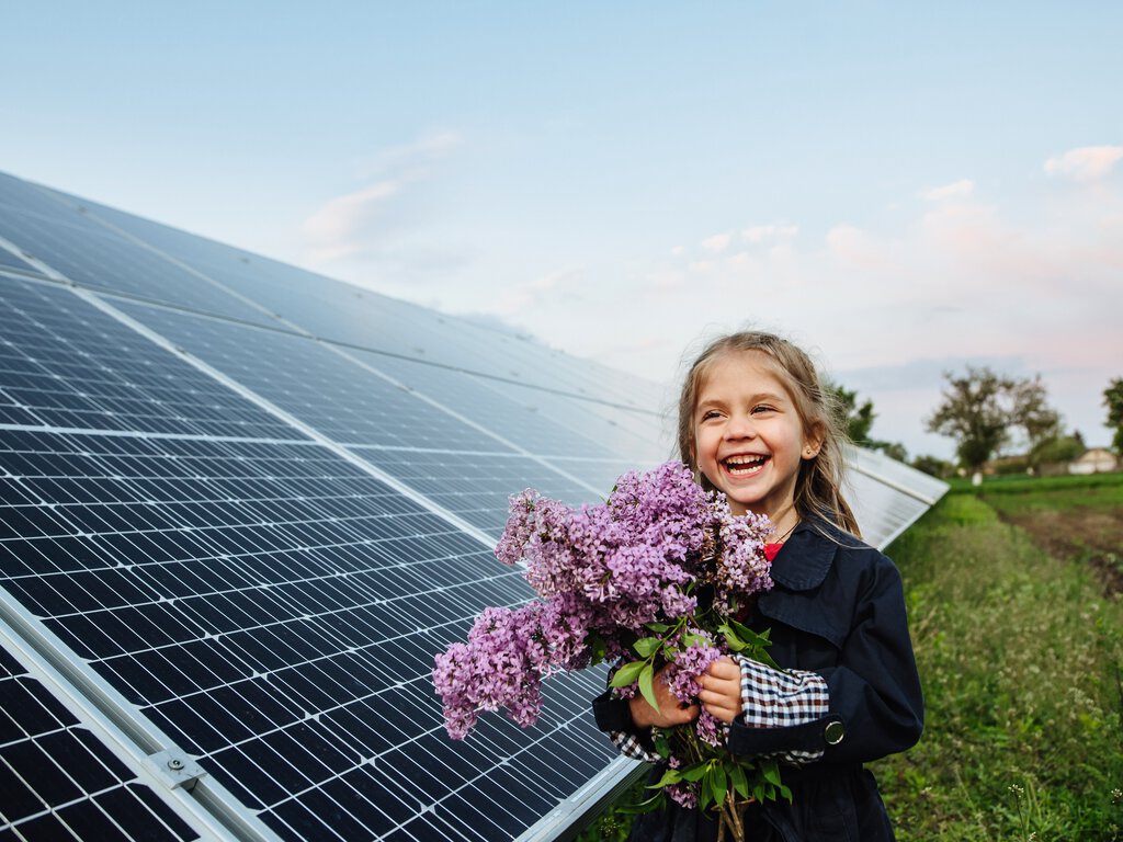 Barn med blomster foran solcellepanel 