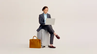 Kvinne på reisefot sitter på en koffert med en laptop