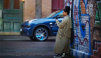 Kvinna står lutad mot tegelvägg med mobil i handen