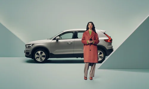 Kvinna i röd jacka står framför en grå bil.