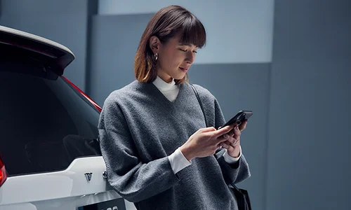 Kvinna i page och grå kläder kollar mobiltelefon.