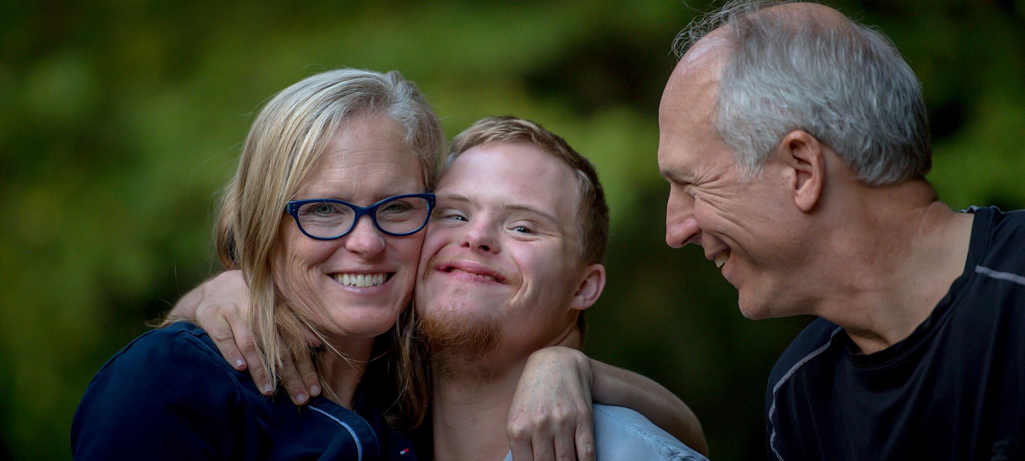 Funksjonshemmet ung mann klemmer mor, far ser på dem, alle smiler