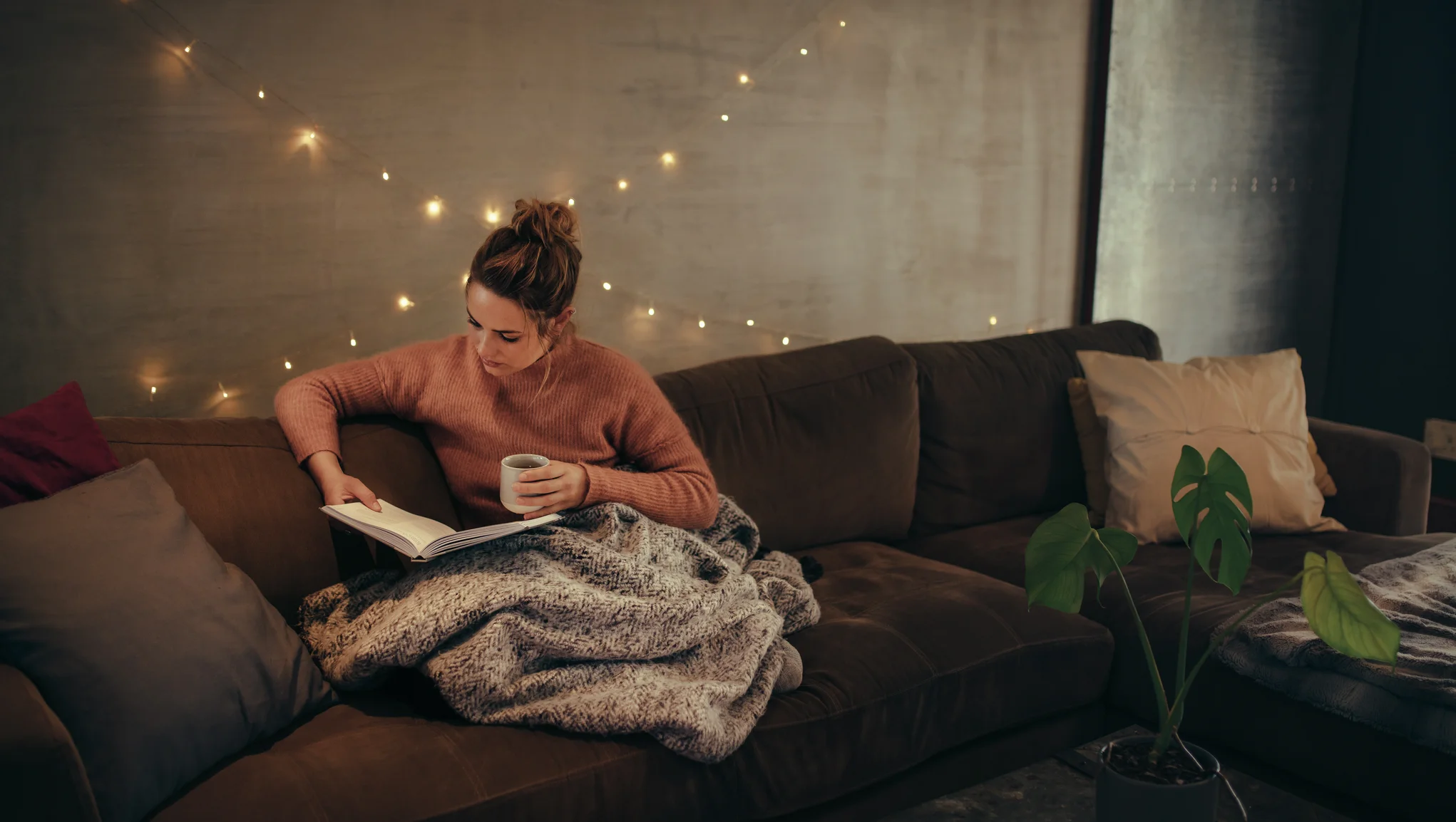 Kvinne sitter i en sofa og leser en bok