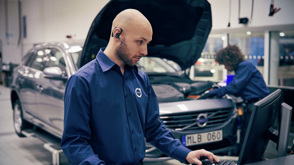 Servicetekniker står vid dator, en annan tekniker inspekterar motorn på en Volvo i bakgrunden