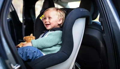 Skrattande pojke sitter i bakåtvänd bilbarnstol.