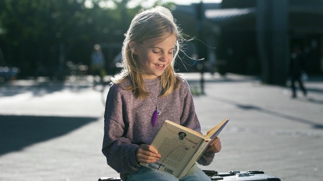 Sommerles: jente som leser bok på koffert