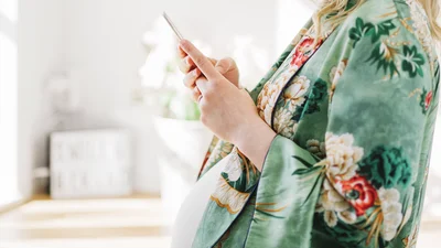 Gravid kvinne i morgenkåpe sjekker mobilen