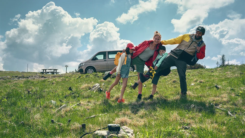 En glad familj står på gräsmattan framför en grå tansportbil.