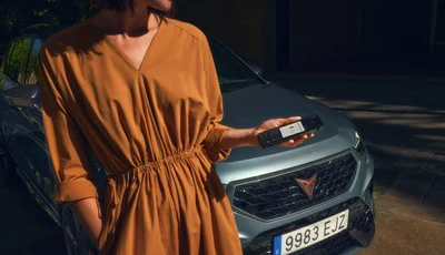 Kvinna i orange klänning kollar mobiltelefon framför en mörk bil.
