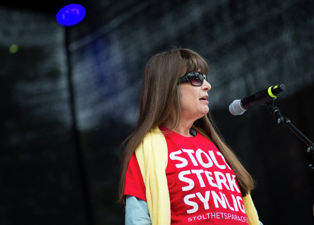 Berit Vegheim på scenen under Stolthetsparaden 2016. Her mottar hun Stolthetsprisen for Stopp Diskrimineringen. Hun snakker i en mikrofon, har langt brunt hår, solbriller og en rød t-skjorte med teksten "Stolt, sterk, synlig!". 
