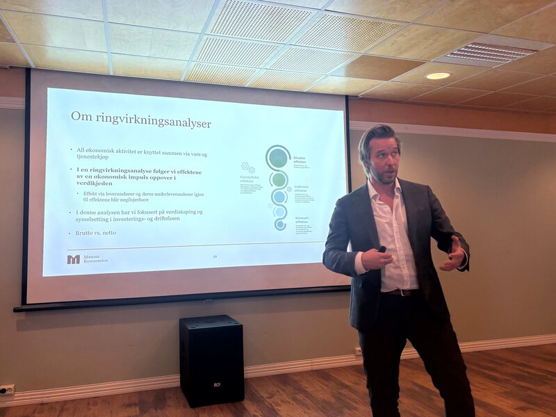 En mann i dress presenterer et norsk PowerPoint-lysbilde med tittelen Om ringvirkningsanalyser fra Menon Economics.