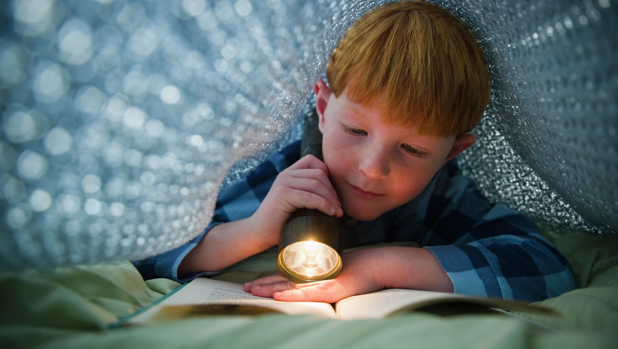 Poika lukee taskulampun valossa kirjaa