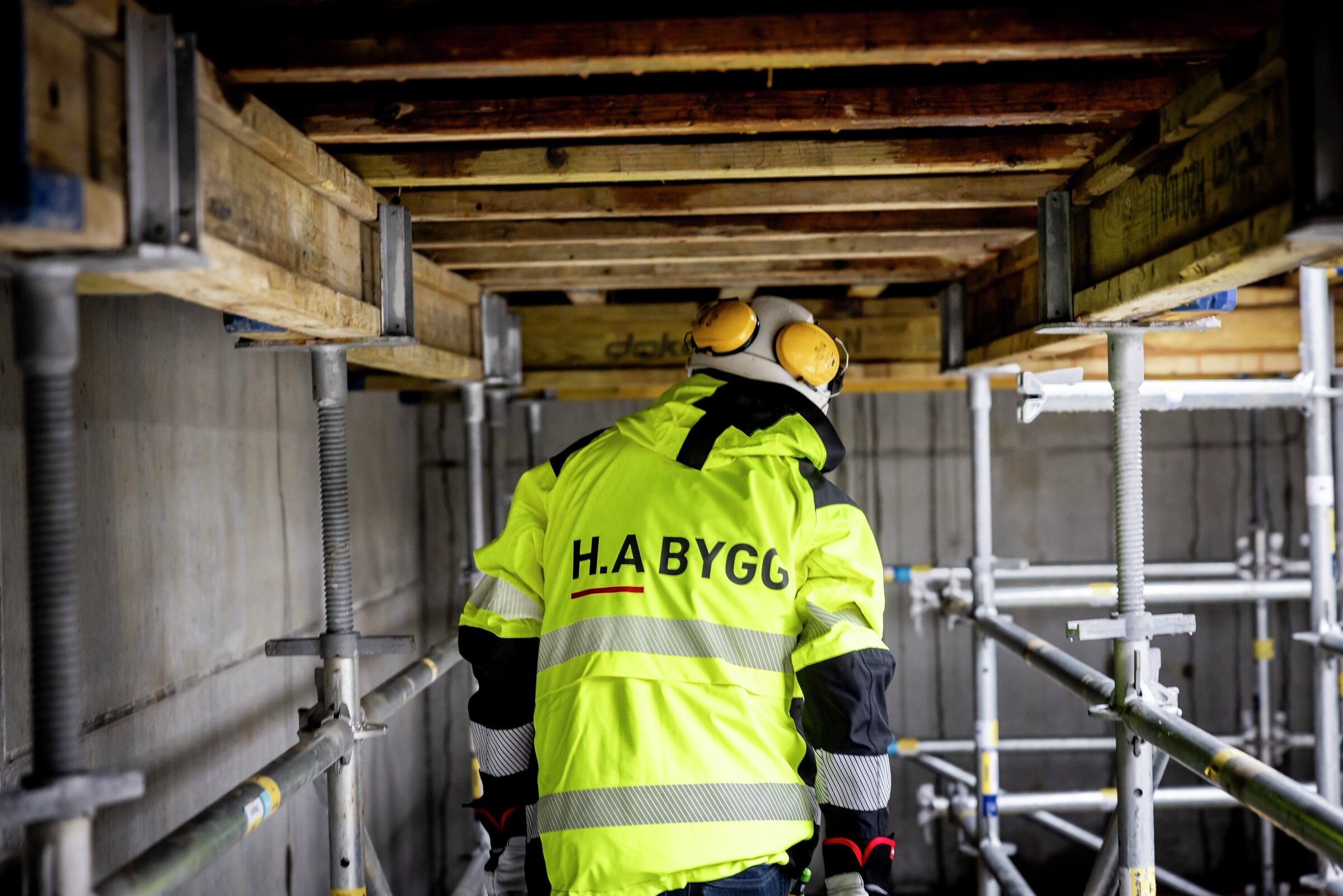 En byggarbetare i gul varselväst arbetar på en byggnadsställning på en byggarbetsplats.