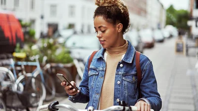 Ung kvinne står med telefon og en sykkel i en by