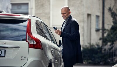 Man med mobiltelefon i handen står vid passagerarsidan av en Volvo XC60