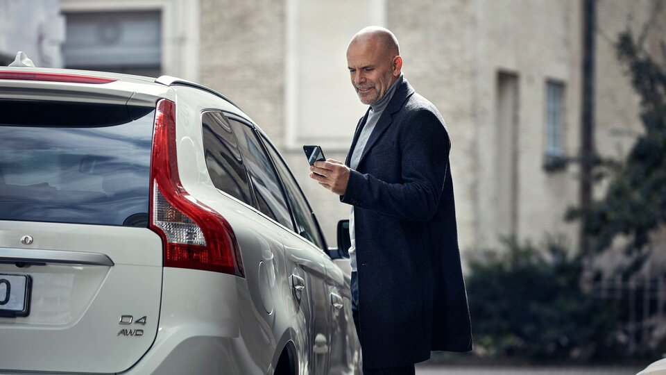 Man med mobil står vid passagerarsidan av Volvo XC60 