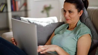 Kvinne sitter i en sofa med en laptop på fanget