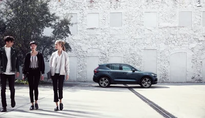 Tre personer går från en Volvo XC40 som står parkerad framför en vit stenvägg.