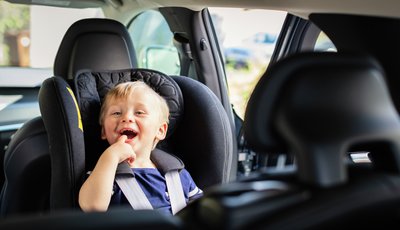 Skrattande pojke i bakåtvänd bilbarnstol