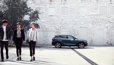 Tre personer går från en Volvo XC40 som står parkerad framför en vit stenvägg.