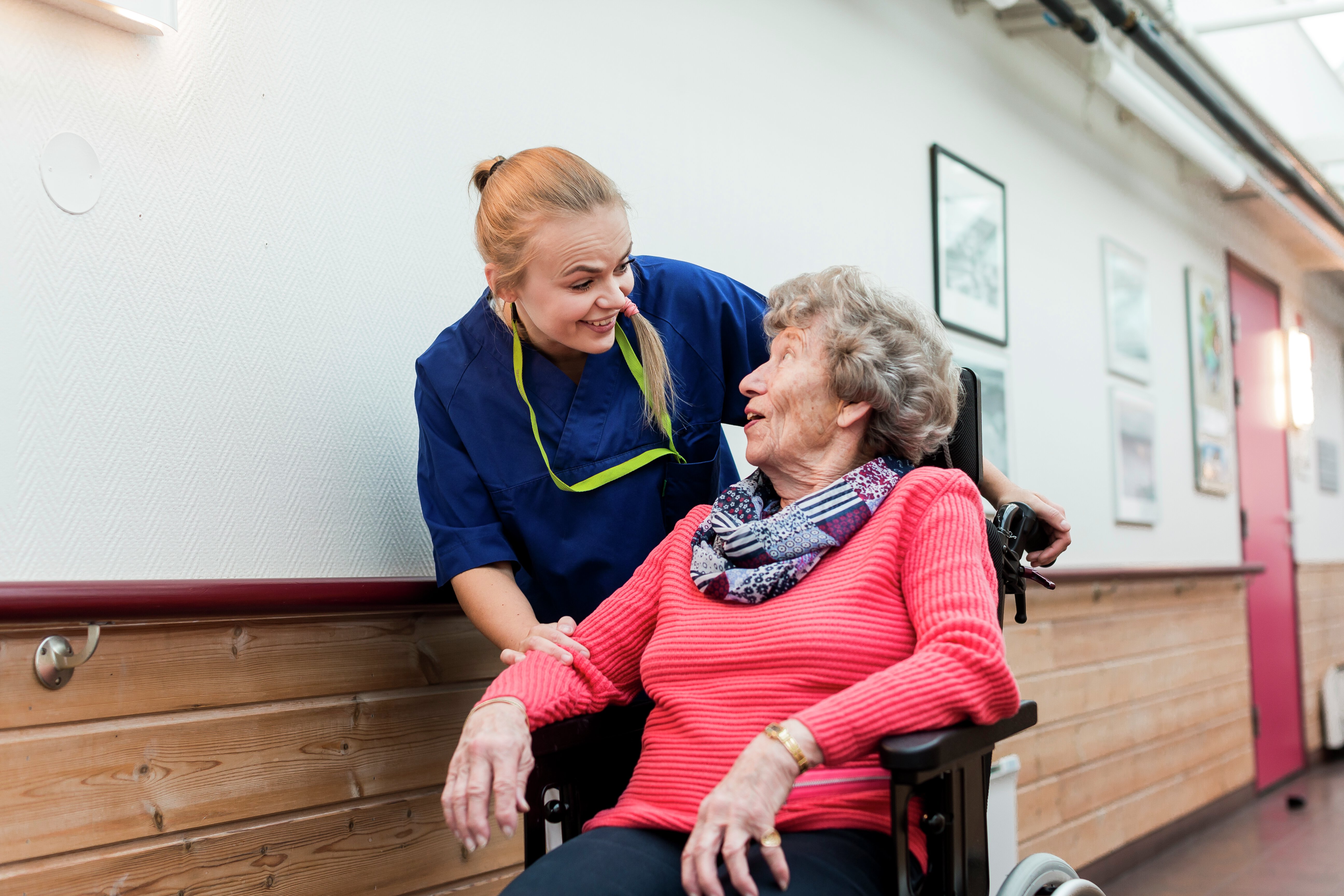 Kvinnelig helsepersonnel med eldre kvinne i rullestol. Foto