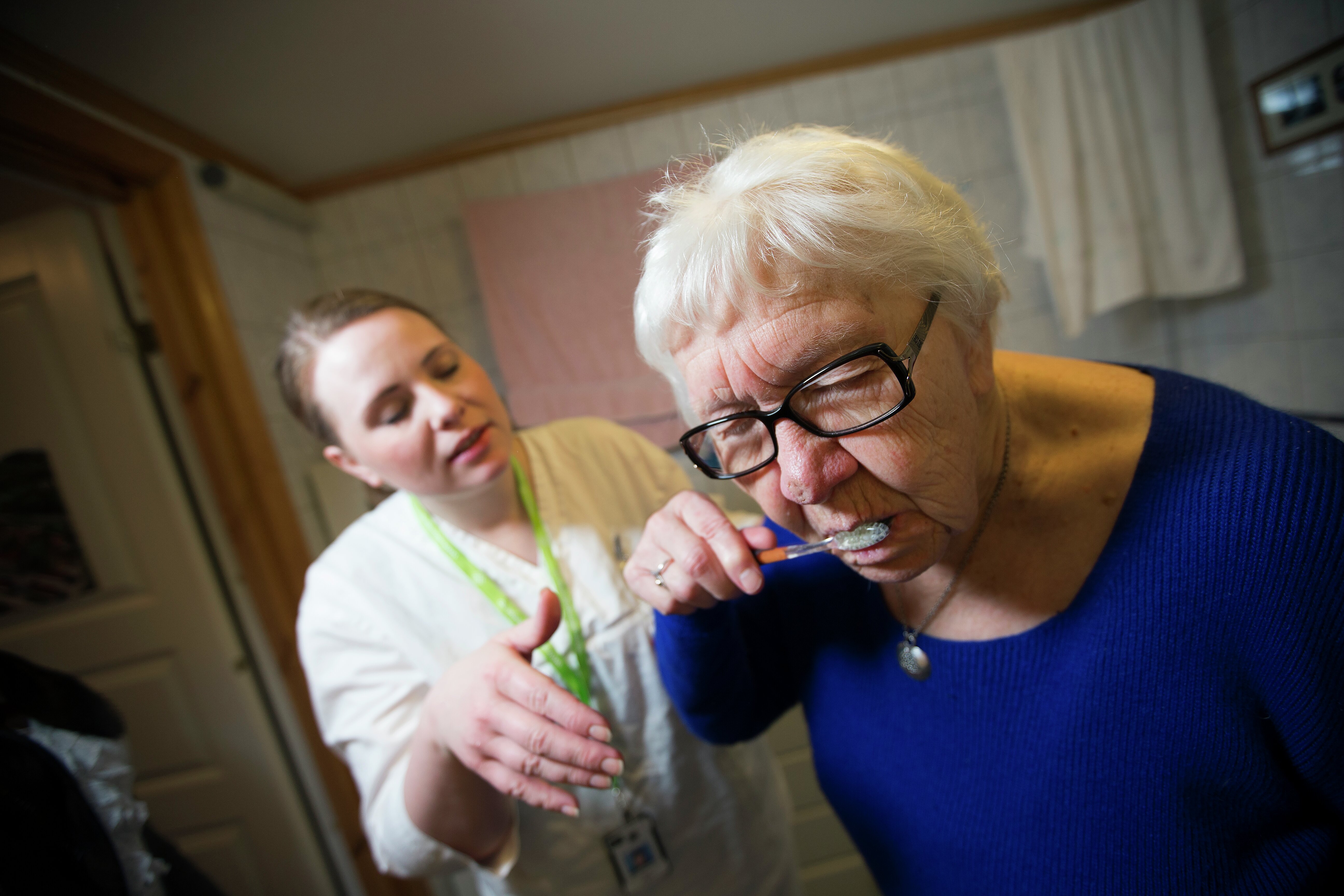 Kvinnelig helsepersonell hjelper eldre kvinne med å pusse tennene. Foto