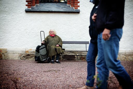 Eldre kvinne sitter på benk mens folk går forbi. Illustrasjonsfoto