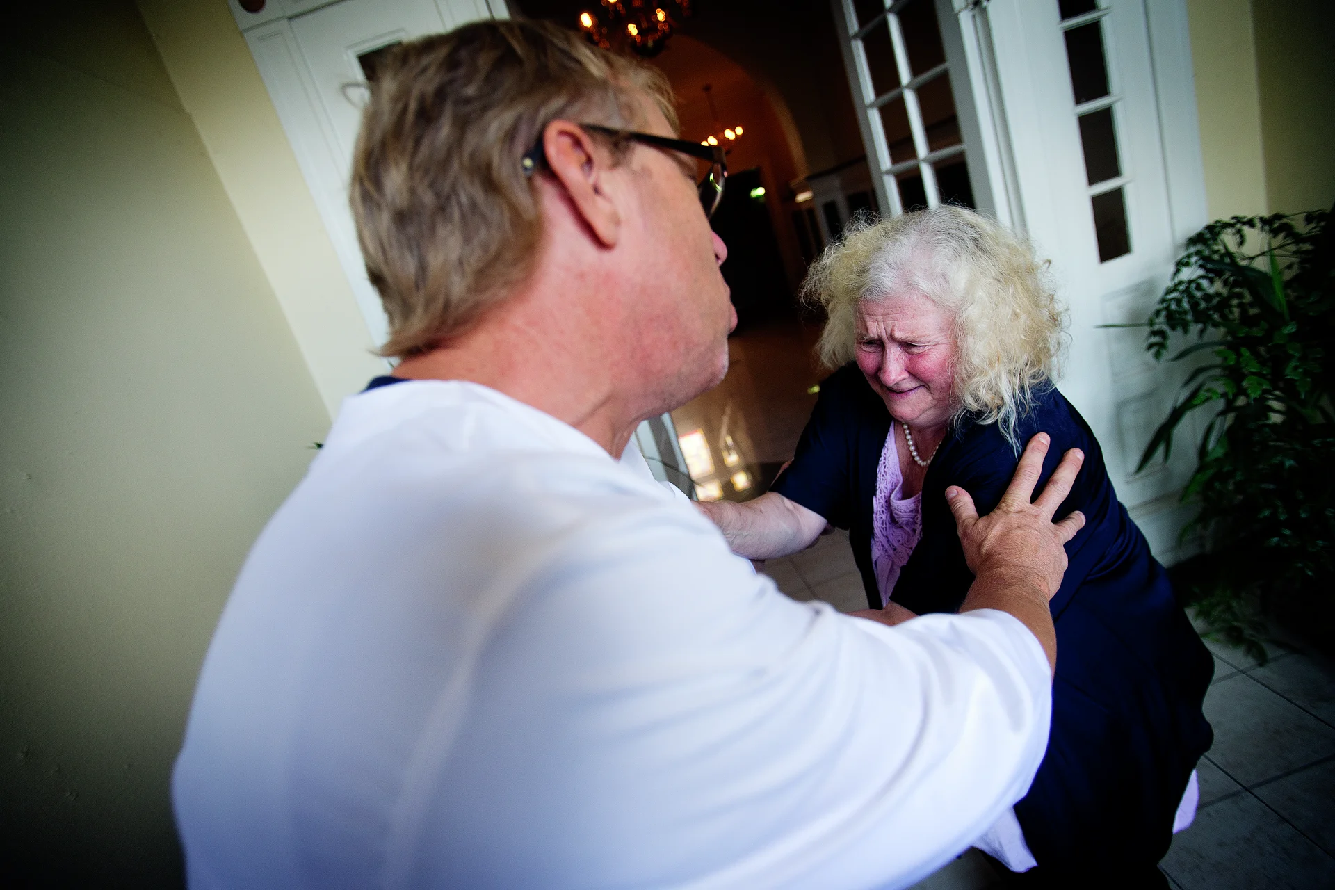 Eldre kvinne i klammeri med mannlig helse- og omsorgspersonell. Foto