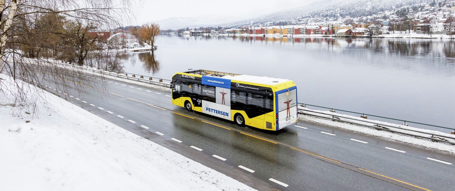 Buss med reklame på siden kjører langs Drammenselva en vinterdag.