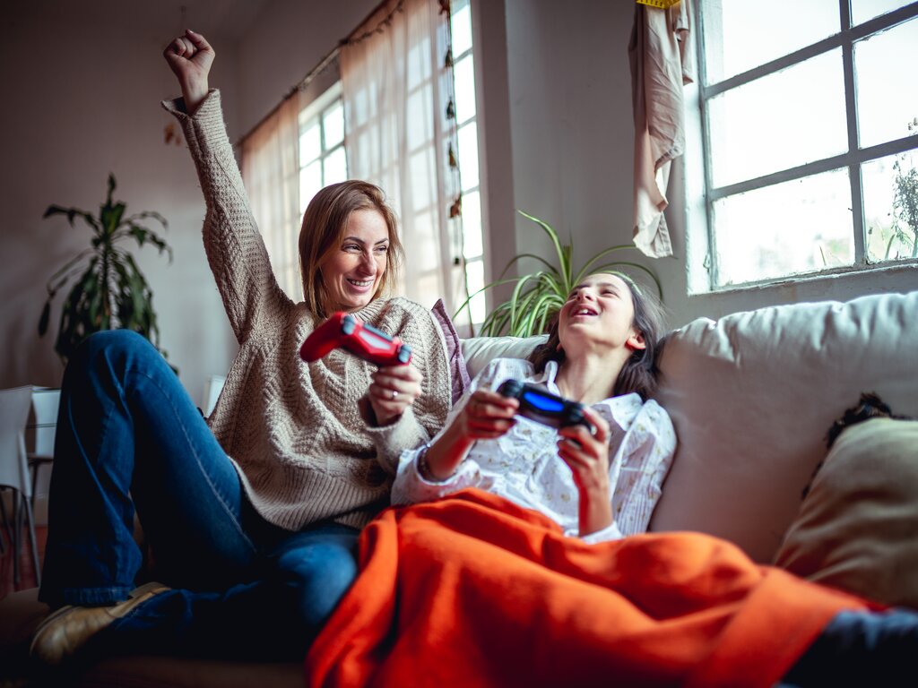 To personer spiller videospill på en sofa, den ene løfter armen i seier, begge smiler og koser seg.