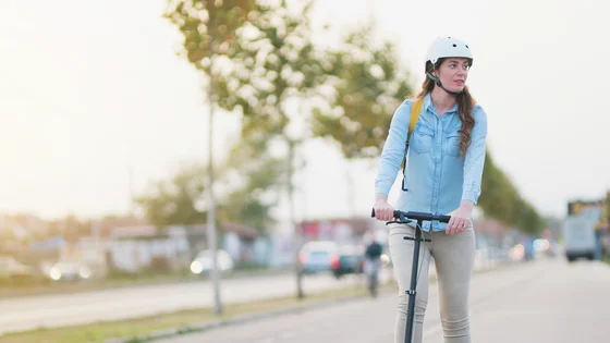 Jente med hjelm står på en sparkesykkel