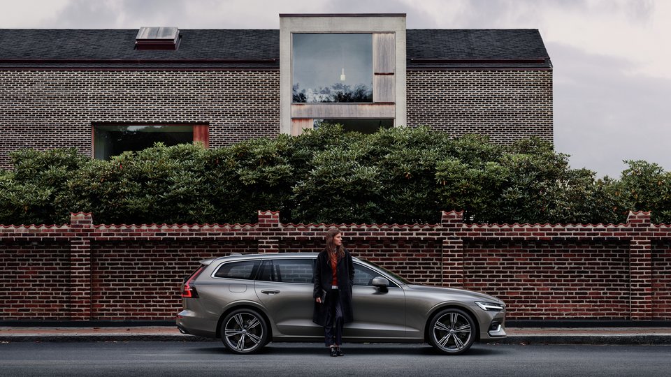 Kvinna står lutad mot en Volvo V60 metallic på gatan