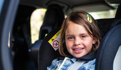 Leende flicka fastspänd i bakåtvänd bilbarnstol