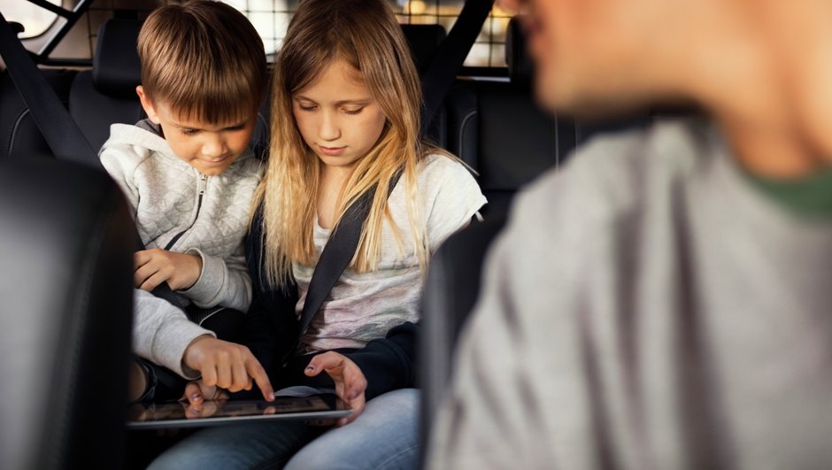 Dreng og pige sidder på bagsædet med en iPad