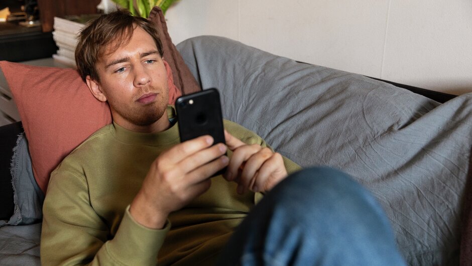 Ung man med mobil ligger på en soffa
