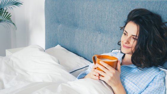 Nainen istuu sängyssä kahvikuppi kädessään