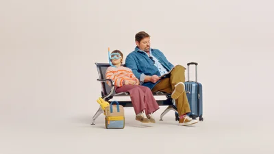 Mies ja lapsi istuvat matkatavaroidensa ympäröimänä