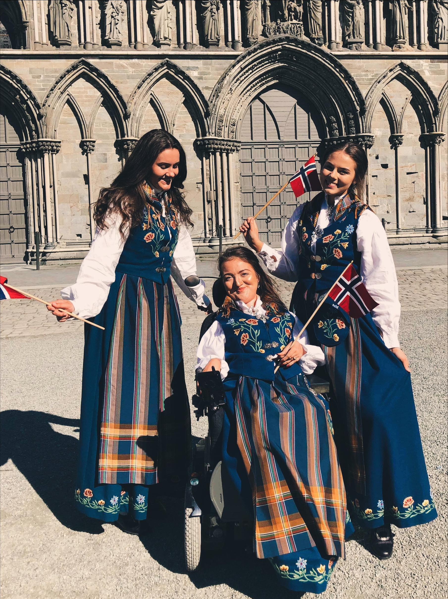 Ingeborg og hennes venner foran Nidarosdomen, i bunad og norske flagg svaiende. Jentene smiler og er glad. 