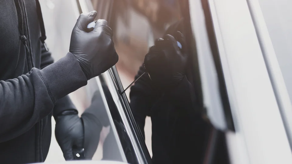Person med svarta latexhandskar gör inbrott i bil via bilrutan.