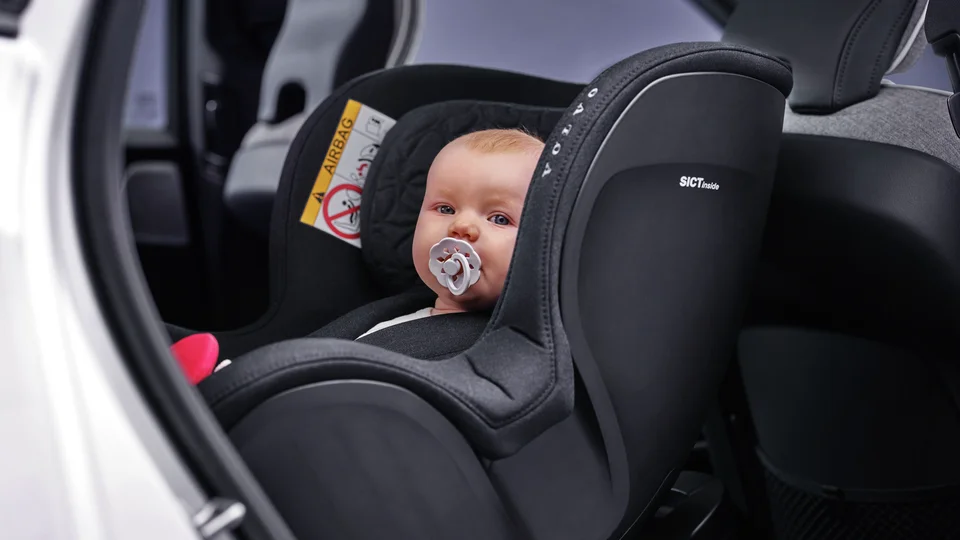 Bebis med napp sitter i bakåtvänd bilbarnstol.