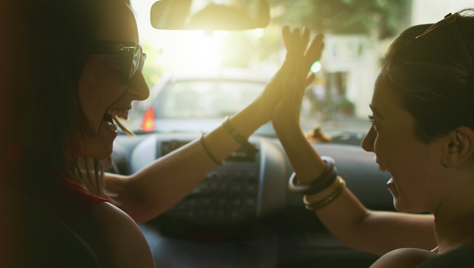 Två unga kvinnor gör high-five i en bil