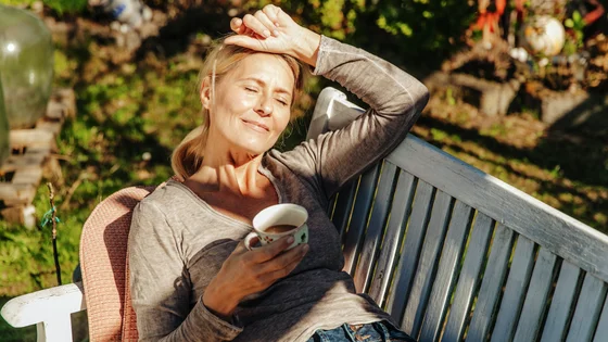 Kvinne drikker kaffe på en benk i solen