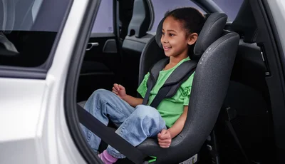 Flicka i grön t-shirt sitter i bakåtvänd bilbarnstol.