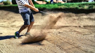 Mies lyö golfpalloa hiekkaesteessä