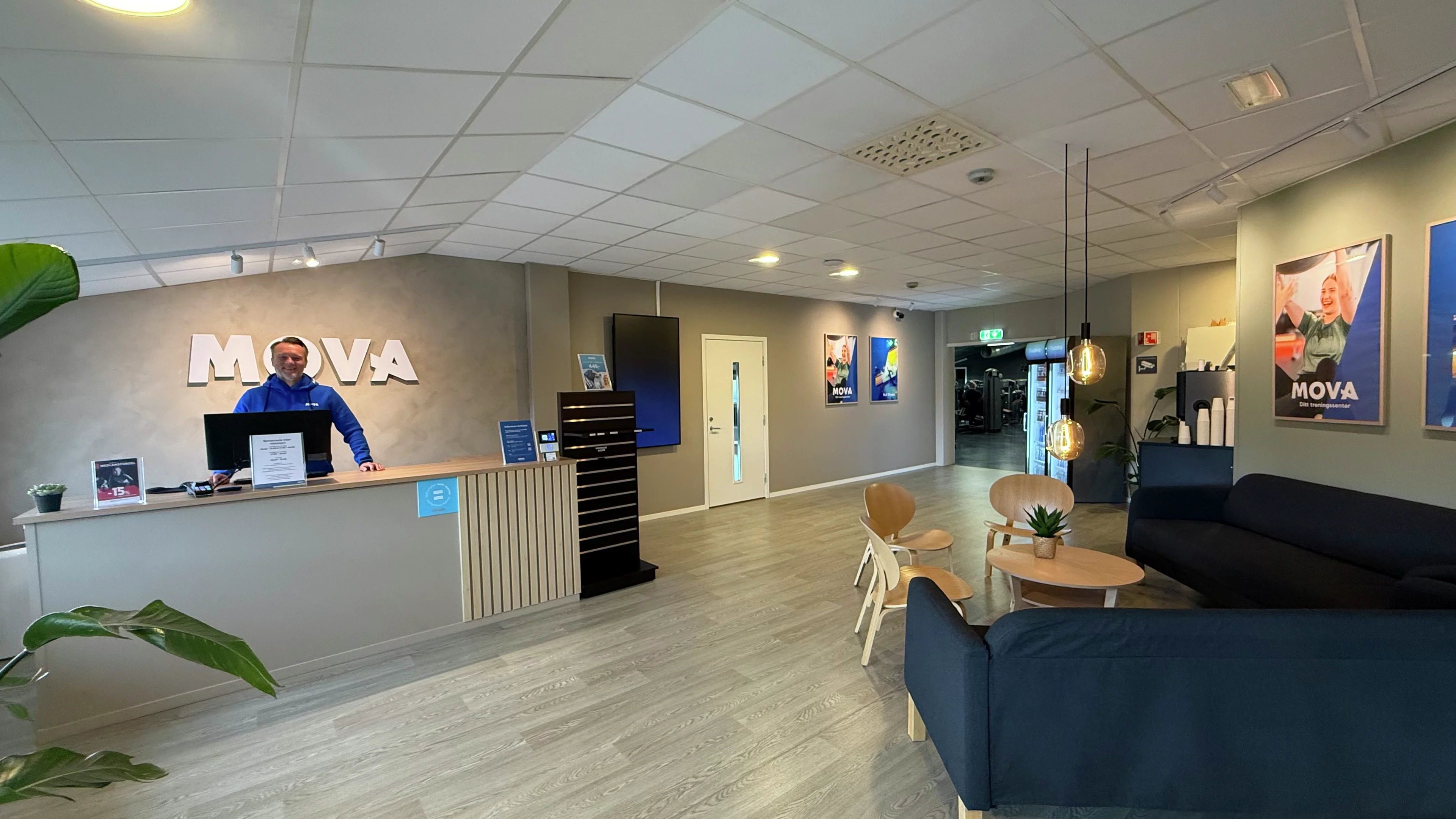 Ansatt ved resepsjonsdisken med MOVA-logo og loungeområde med sofaer på MOVA Mathopen.