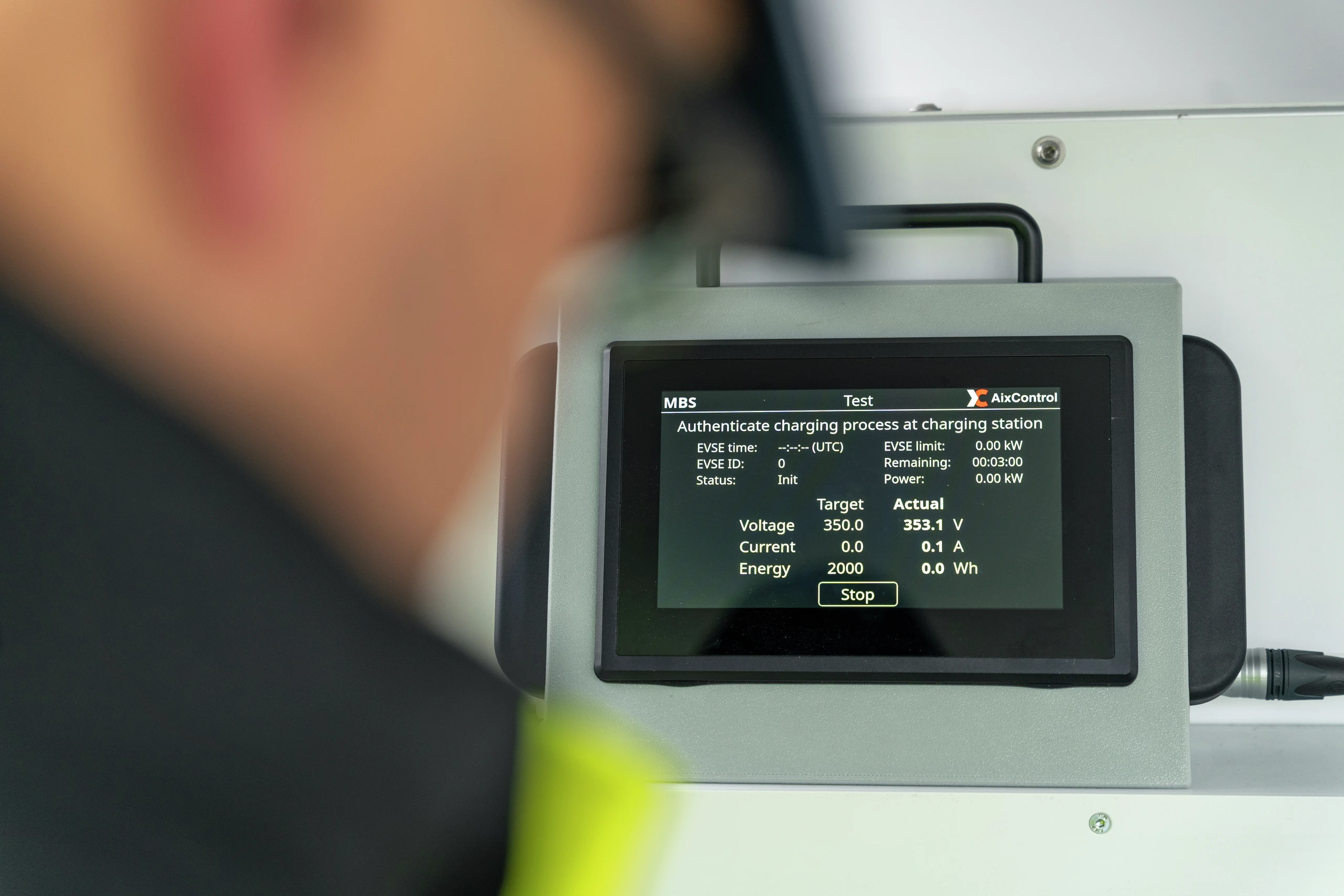 En tekniker ser på en AlxControl MBS-testenhet som viser autentiseringsdata for ladestasjoner for elbiler med spennings- og strømavlesninger.