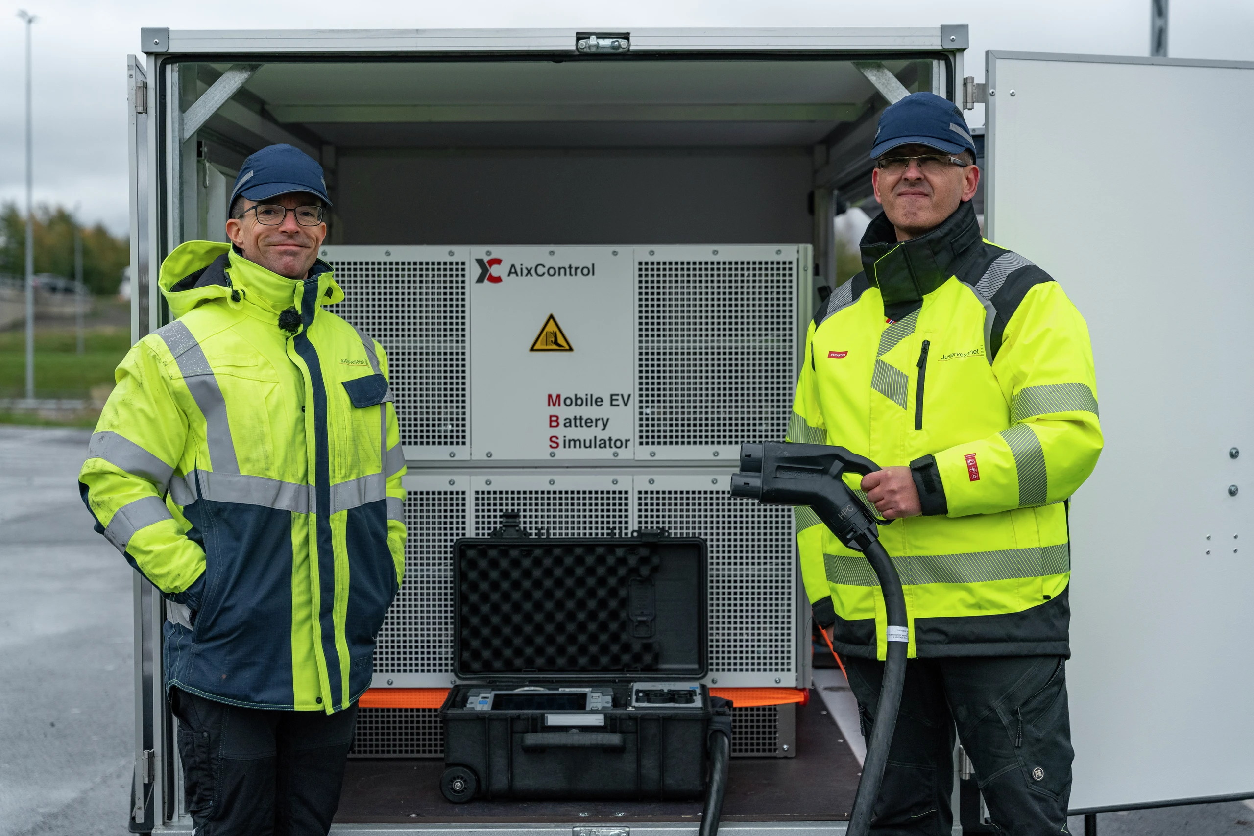 To teknikere i refleksvester står ved siden av en AixControl Mobile EV-batterisimulator i en tilhenger.